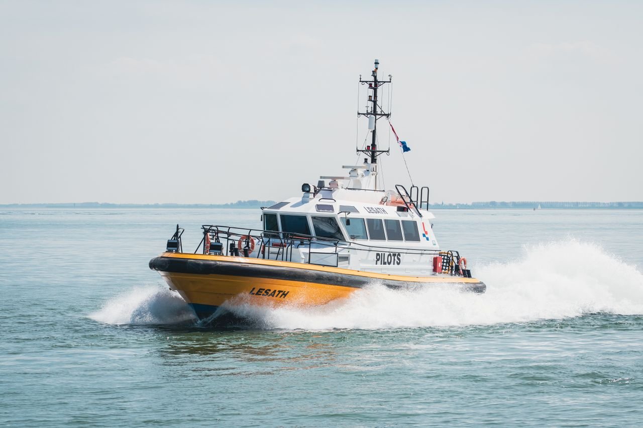 A powerful pilot boat cutting through the water at speed on a clear day in the ocean.